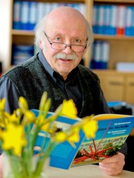 Portraitfoto von Erwin Schütterle, im Vordergrund Osterglocken, Schütterle hält ein Buch in der Hand